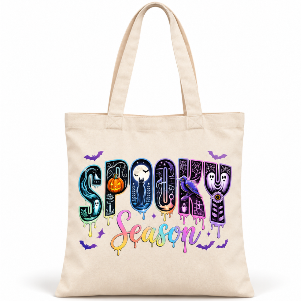 A cream canvas tote bag featuring a colorful 'Spooky Season' graphic print with Halloween-themed lettering and small illustrations of bats, a witch, a ghost, and a pumpkin, shown on a plain white background.