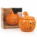 An orange pumpkin-shaped ceramic oil burner and wax warmer with a lid, shown in front of its product box on a white background.