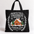 A black canvas tote bag with a festive Christmas-themed graphic for 'North Pole Gingerbread Bakery'. The design features white text reading 'North Pole Gingerbread Bakery', 'Merry Xmas', and 'Bakery Club Always Fresh', surrounding an illustration of a gingerbread house, snow, pine trees, and stars, set against a clean white background.