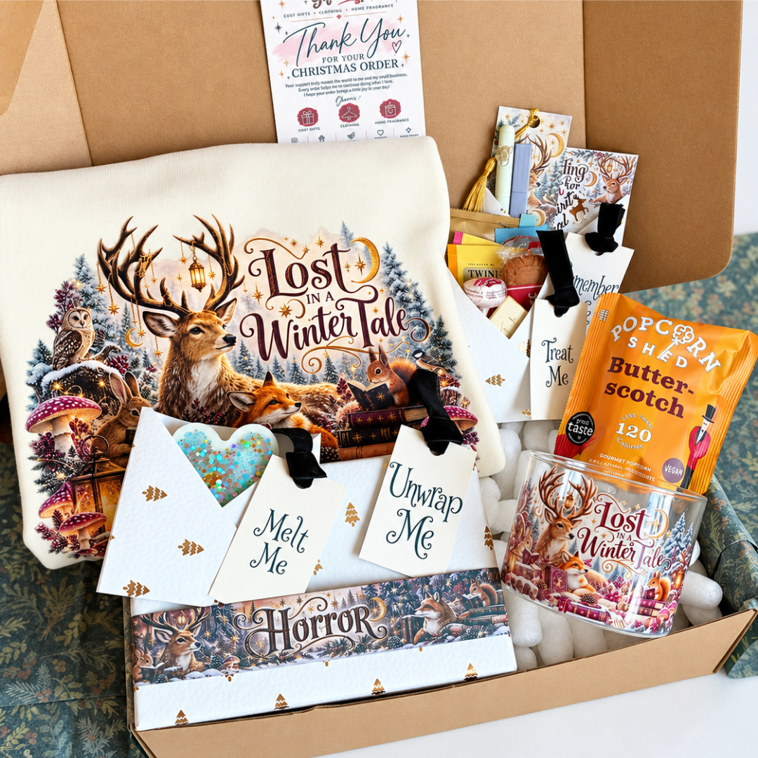 A curated Christmas gift box filled with themed items, including a large cream tote bag printed with a deer and winter scene, a glass mug, a bag of popcorn, small cards, and tags, all arranged in a cardboard box.