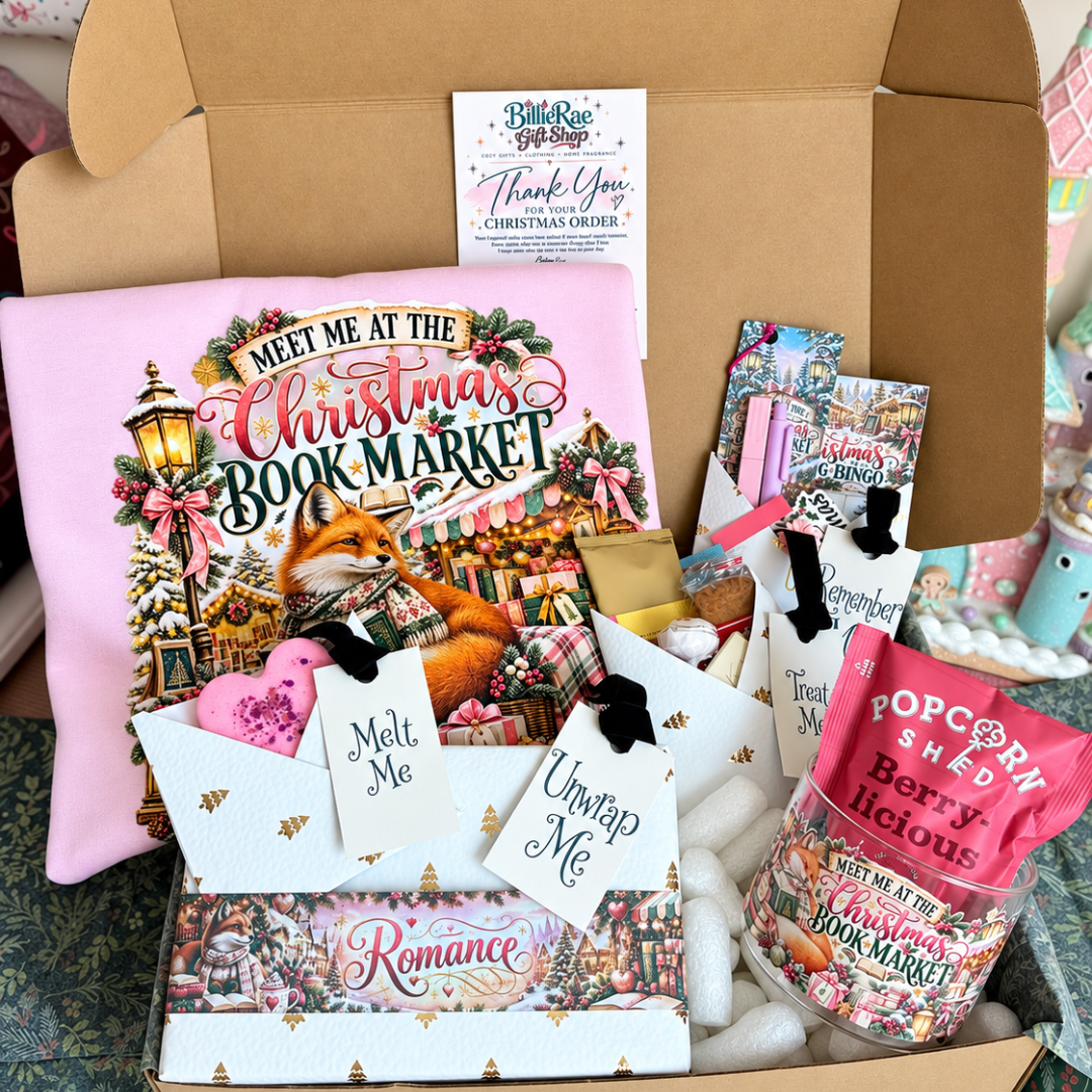 A curated gift box filled with themed items from BlueRose Gift Shop, featuring a pink 'Meet Me at the Christmas Book Market' pillow, a romance novel, candy, and handwritten gift tags.