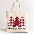 A natural canvas tote bag with a festive Christmas design featuring three red and white buffalo plaid Christmas trees and the words 'Merry Christmas' in black script.