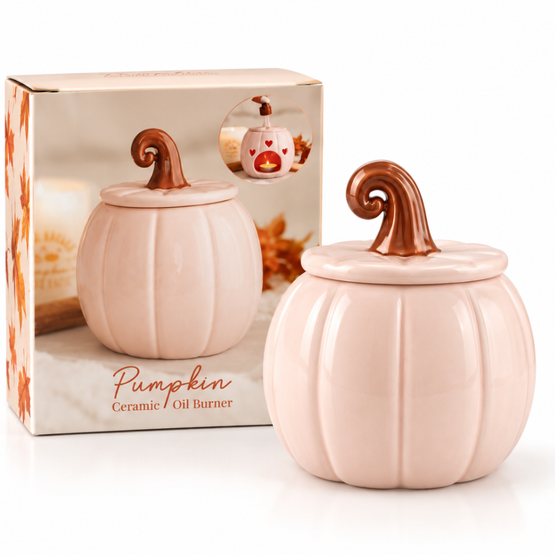 A ceramic pumpkin-shaped oil burner shown in front of its retail box. The burner is a pale blush pink with a ribbed pumpkin body and a curled copper-brown stem.