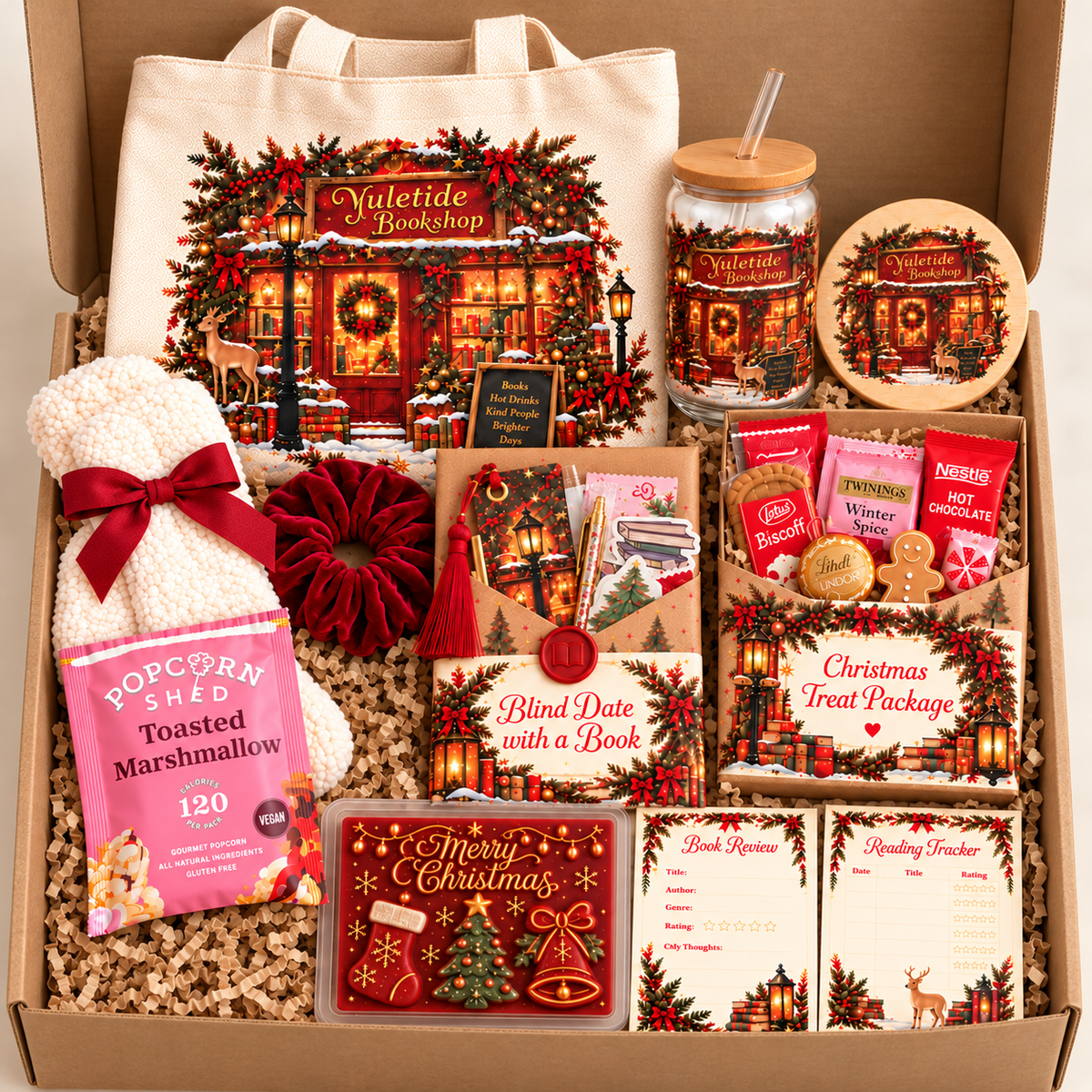 A curated Christmas gift box set from Yuletide Bookshop, featuring a cream canvas tote bag, a jar with a lid, a round wooden coaster, marshmallows, a pink popcorn bag, a red flower, and multiple holiday-themed cards and bookmarks arranged in brown crinkle paper inside a cardboard box.