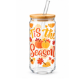A clear glass tumbler with a bamboo lid and clear glass straw, decorated with autumn illustrations and the text 'Tis the Season' in orange and yellow lettering.